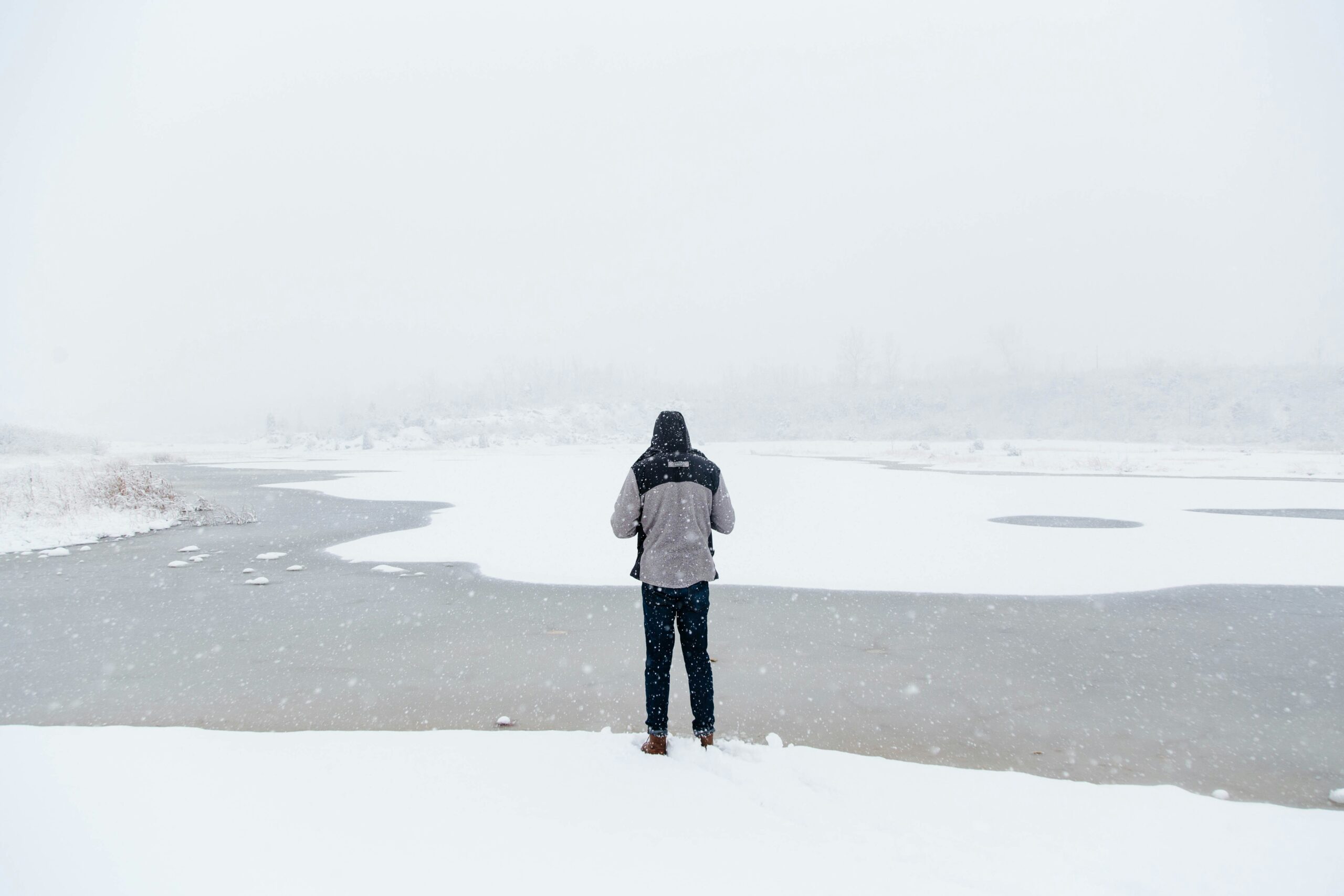 Image of a man looking at a ice and snow covered river in a snow storm.